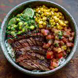 A bowl of food with meat, rice, tomatoes, corn, and lime.