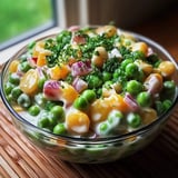 A bowl of food with peas and corn.