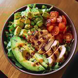 A bowl of food with chicken, avocado, tomatoes, and lettuce.