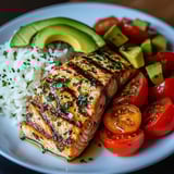 A plate of food with fish, rice, and tomatoes.