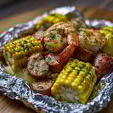 A plate of food with shrimp, corn, and sausage.