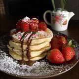 A plate of pancakes with chocolate syrup and strawberries.