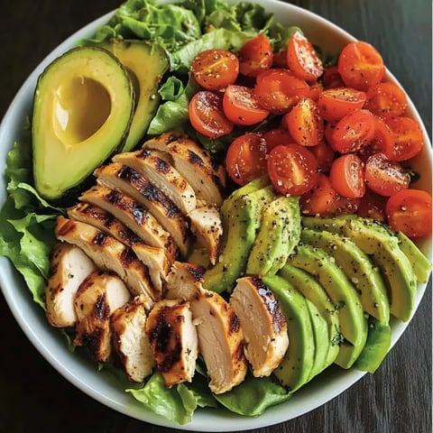 A bowl of food with chicken, avocado, tomatoes, and lettuce.
